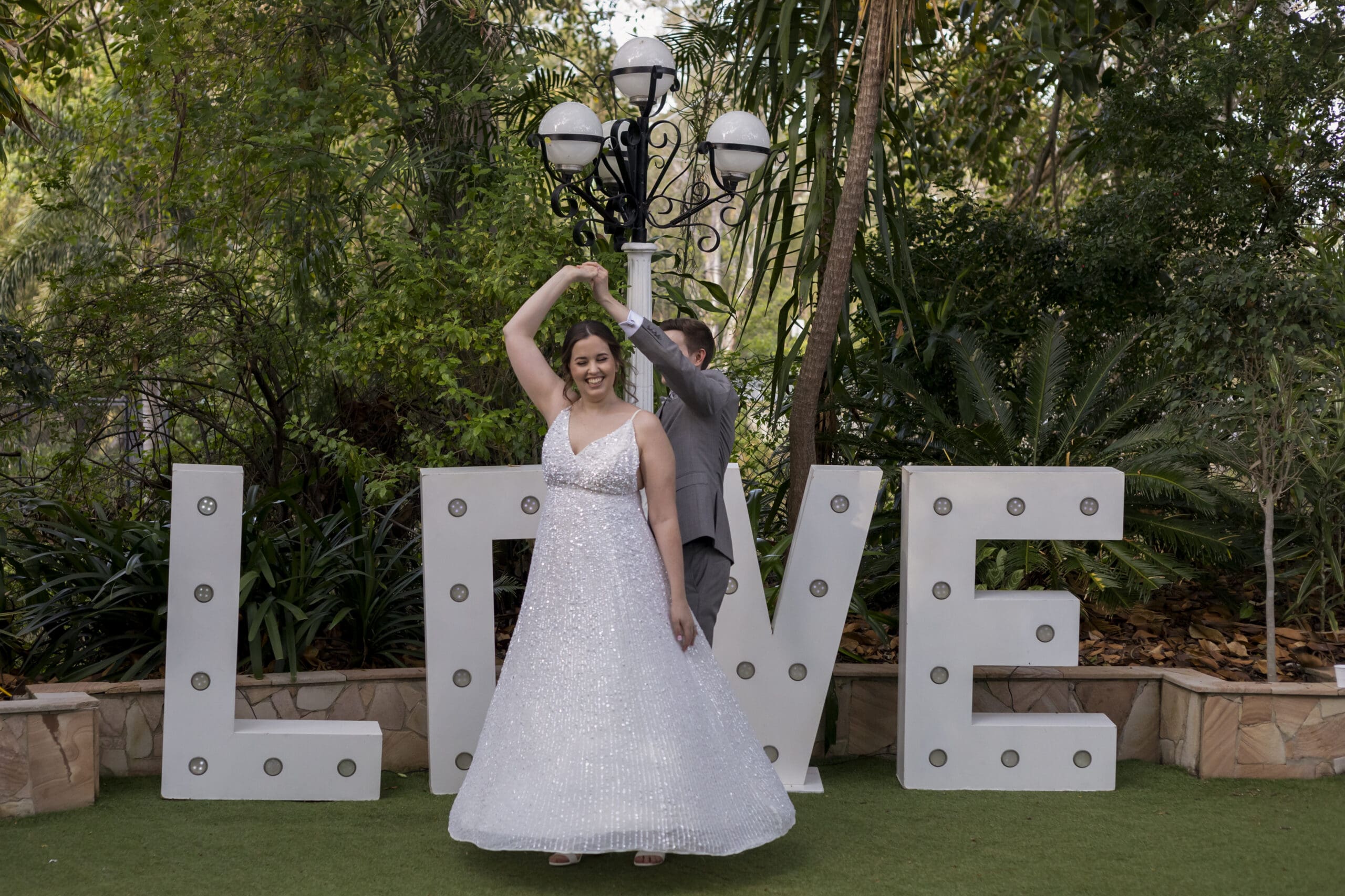 Bride in A Line dress being twirled by husband in front of 'LOVE' sign.