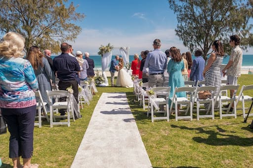 A newly wed couple sharing their first kiss at a beachside loaction in Perth. All their guests are standing and watching.
